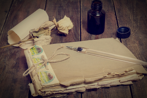 Composition in retro style: old battered notebook, ink bottle, pen, dried rose and a yellowed sheet of paper. Tinted photos