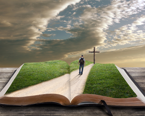 An open bible with grass and a man walking towards a cross