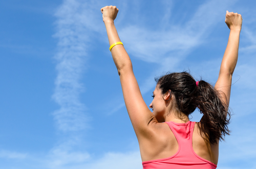 Woman from behind with arms raised expressing success towards sky on a sunny summer day.