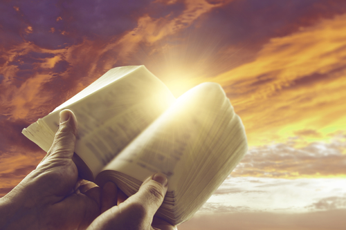 Hands holding open book in front of sky