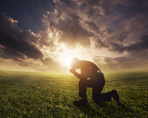 Silhouetted man praying at sunset